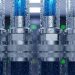 Close-up of four thick, metallic cables with blue cores, droplets, and a data center blurred